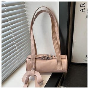 Dettaglio della borsa cilindrica in pelle rosa con tracolle lunghe e ciondolo a fiocco