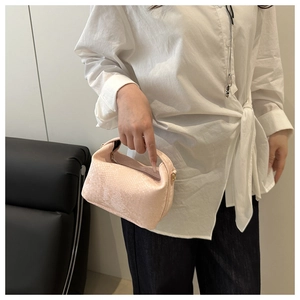Detail of pink snake-embossed pillow bag with gold hardware held by a model in white shirt