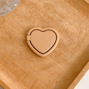 Close-up of a minimalist beige heart-shaped phone ring stand on a wooden background