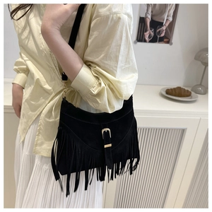 Detail of a vintage black suede fringe crossbody bag with gold hardware on a model