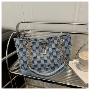 Close-up of checkered denim tote bag with frayed edges and golden deer charm