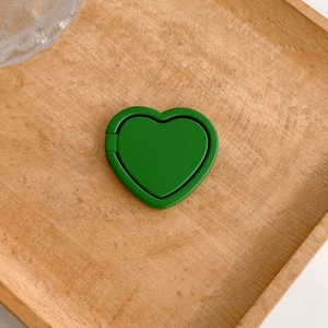 Close-up of vibrant green heart-shaped phone ring holder resting on a wooden tray