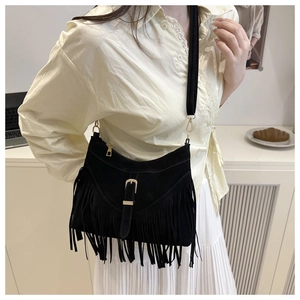 Detail of black suede shoulder bag with long fringes and gold buckle on a wide strap