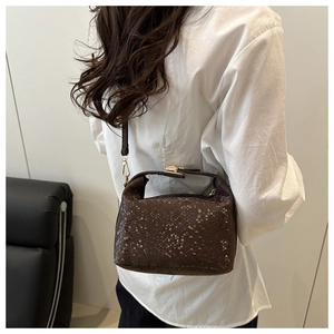 Detail of dark brown python-texture pillow bag with gold metal hardware on a model