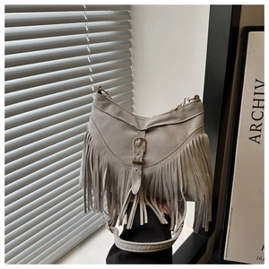 Close-up of grey suede crossbody bag featuring long fringe tassels and buckle detail