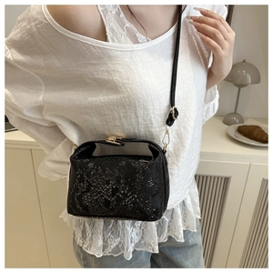 Detail of black snakeskin texture handbag with gold metal clasp on a crossbody strap