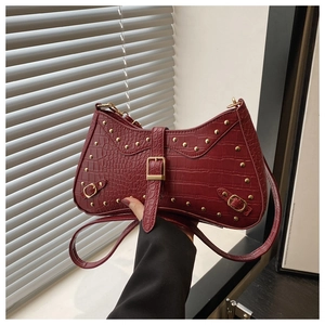 Detail of dark red crocodile pattern handbag with gold rivets and buckle strap