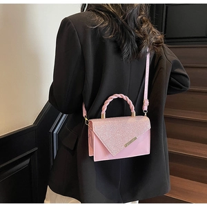 Sac à bandoulière rose à paillettes porté par un mannequin avec un blazer noir