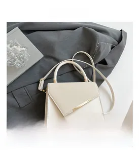 Détail d'un sac à main structuré en cuir crème avec garniture dorée sur une veste