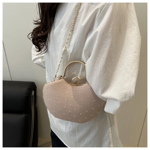 Detail of pink heart-shaped bag with textured fabric, gold chain, and rhinestone closure