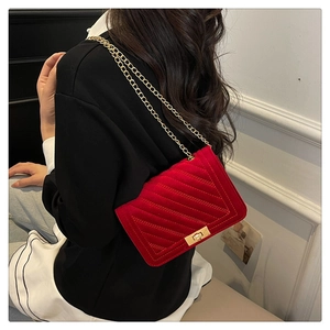 Detail of red velvet crossbody bag with golden chain strap and chevron quilting shown on model