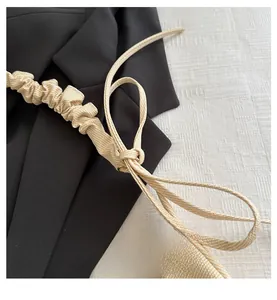 Close-up of beige pleated underarm bag with woven texture on a dark blazer