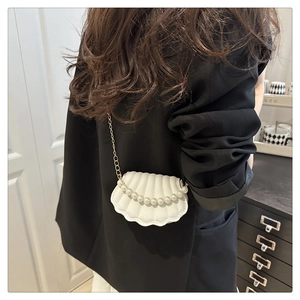 Detail of cream-white shell bag with pearl handle and golden chain on a black jacket
