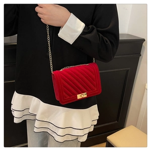 Detail of red velvet crossbody bag with quilted texture and gold metal chain strap