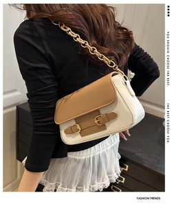 Detalle del bolso bandolera marrón y blanco con cadena dorada y hebillas decorativas