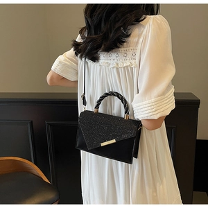 Détail d'un sac à main noir scintillant avec poignée dorée sur robe blanche