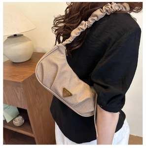 Detail of pleated shoulder strap and triangular metal plaque on a chic apricot crossbody bag