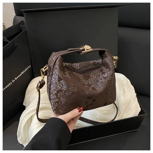 Detailed close-up of dark brown snake-pattern pillow bag with golden clasp and silk box