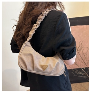 Detail of a beige textured underarm bag featuring a ruched cloud strap and metal logo