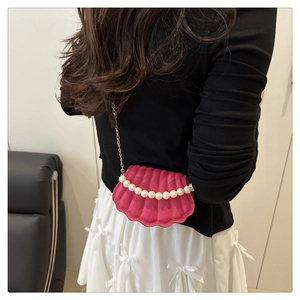 Pink shell-shaped crossbody bag with pearl chain detail and metallic strap on a model