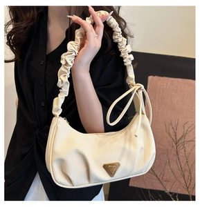Close-up of a cream pleated shoulder bag with ribbon bow and metal triangle plaque