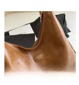 Close-up of brown vintage PU leather texture and gold oval logo plaque on shoulder bag