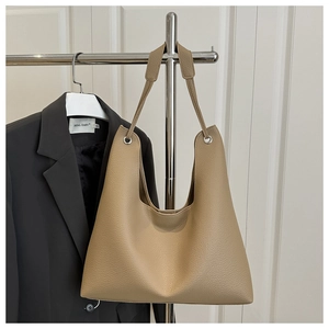 Detail of khaki pebbled leather tote bag hanging on a metal rack with blazer background