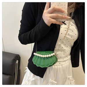 Detail of green shell crossbody bag with pearl trim and gold chain strap on model