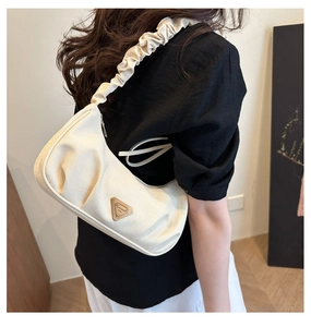 Detail of cream crescent shoulder bag with ruched strap and gold metal emblem