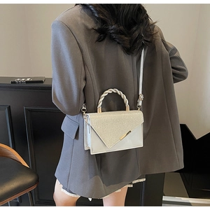 Détail du petit sac argenté pailleté avec poignée métallique sur blazer gris