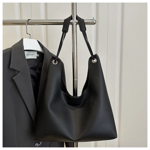 Detail of black lychee grain leather tote bag with silver metal eyelets on a hanger
