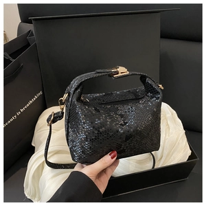 Detail of black snakeskin texture bag with gold metal clasp and detachable strap