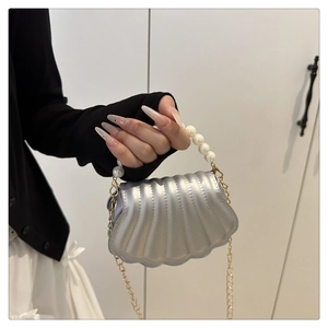 Detail view of a silver shell bag with pearl handle and golden chain shoulder strap