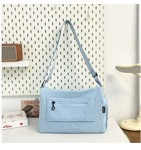 Close-up of light blue canvas crossbody bag showing front zipper pocket and strap detail