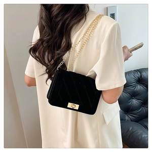 Detail of black quilted crossbody bag with gold chain strap and lock worn by model