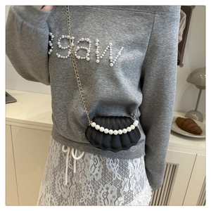 Detail view of mini black shell-shaped crossbody bag with pearl handle and gold chain strap