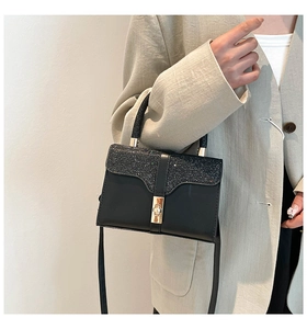 Detail of black glossy sequin handbag flap with elegant gold twist lock and handle