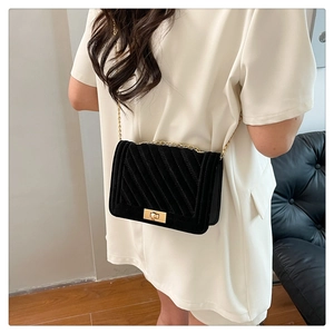 Detail of a black velvet crossbody bag with gold chain and lock worn by a model