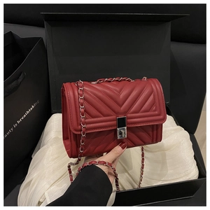Détail d'un sac bandoulière en cuir matelassé bordeaux avec chaîne argentée et boîte cadeau
