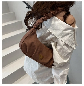 Close-up of brown ruched shoulder bag with textured fabric and metallic triangle logo