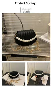 Detail of black shell bag featuring wavy pleats, white pearls, and gold chain strap