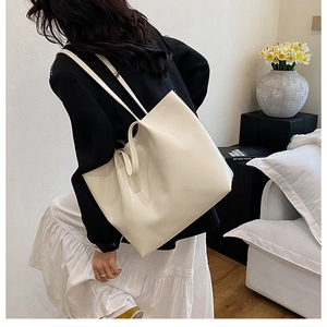 Minimalist cream tote bag styled on model shoulder in a cozy interior setting