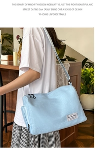 Detail of light blue canvas crossbody bag showing dual zippers and brand logo tag