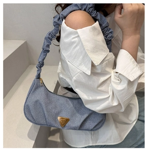 Macro shot of light blue denim baguette bag with pleated handle and metal triangle plate