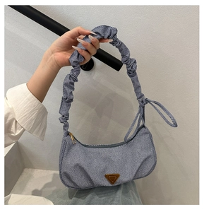 Detailed shot of denim shoulder bag featuring ruched handles and metal triangle plaque