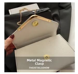 Detail of white glitter handbag featuring a V-shaped gold metal trim and magnetic snap