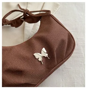 Détail d'un sac porté épaule tissé marron avec ornement de papillon en métal argenté