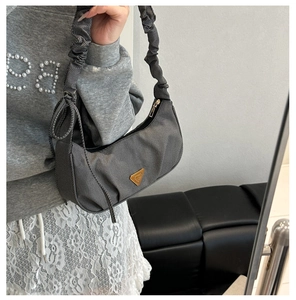 Macro view of grey fabric shoulder bag showing pleated strap and gold triangle ornament