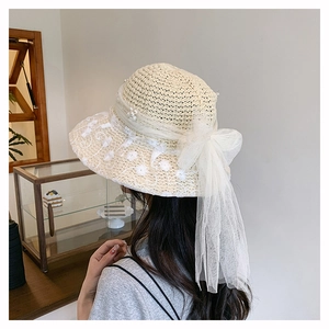 Detail of elegant beige woven straw hat featuring floral lace embroidery and mesh bow with pearls