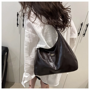 Detail of a dark brown soft leather tote bag with a gold oval metallic fashion emblem